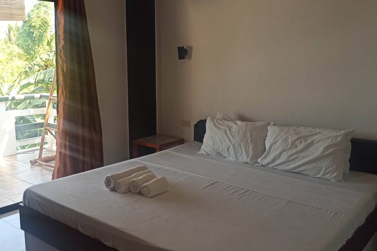 A hotel room with a bed, a nightstand, a window with curtains, and an air conditioning unit on the wall.