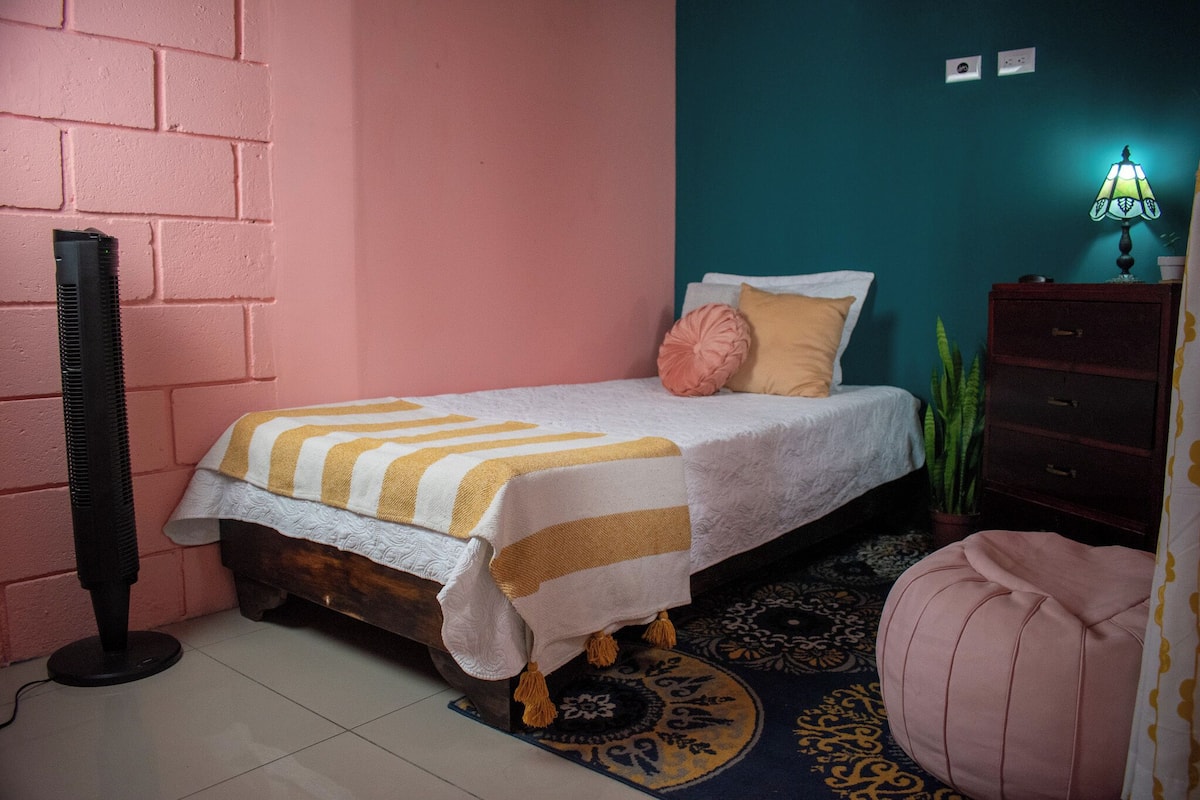 Un dormitorio con cama, mesita de noche, lámpara y planta en maceta.