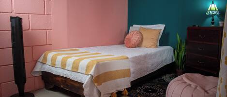 A bedroom with a bed, a nightstand, a lamp, and a potted plant.