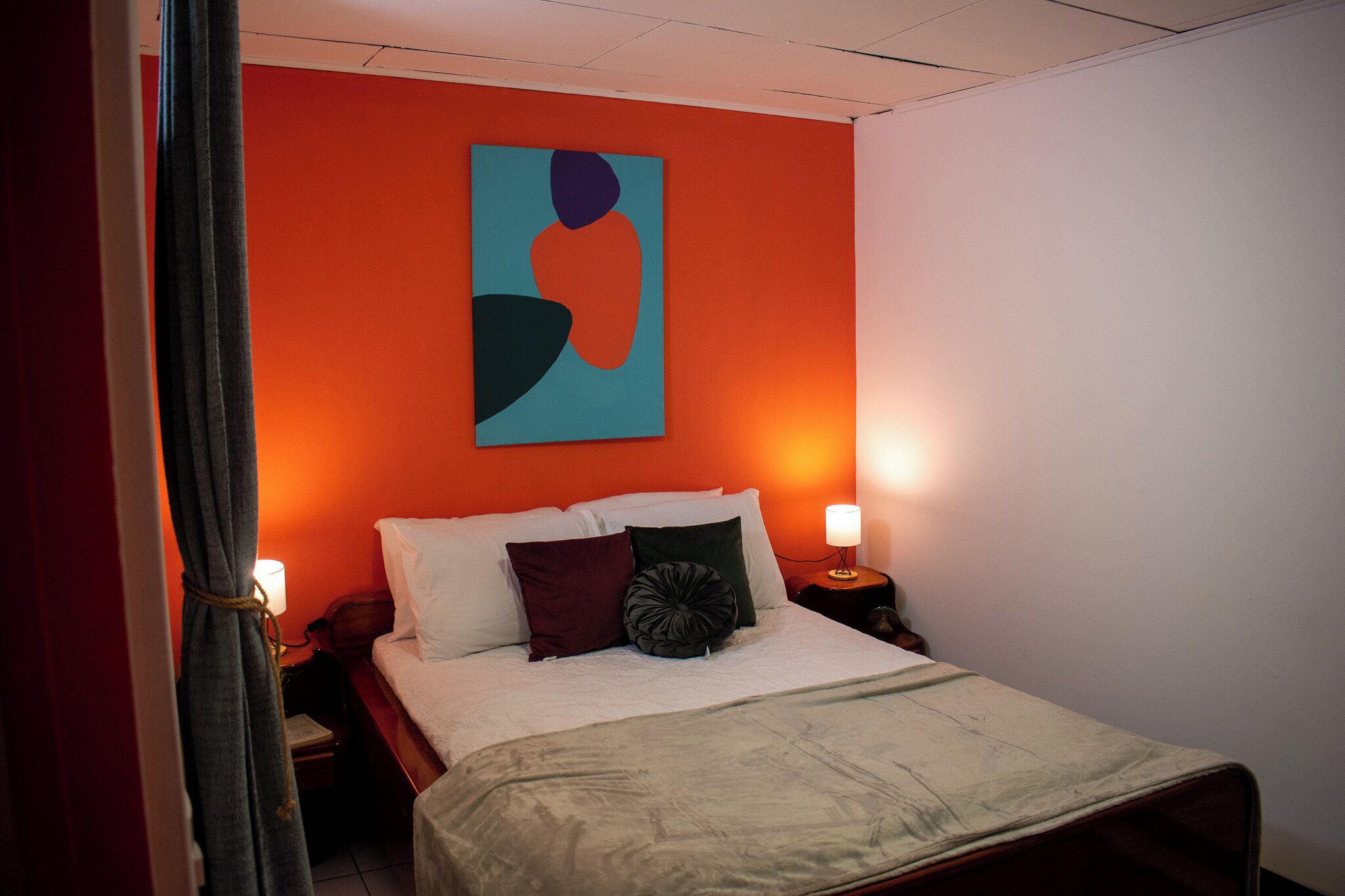 A hotel room with a bed, a nightstand, a lamp, and a painting on the wall.