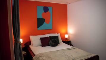 A hotel room with a bed, a nightstand, a lamp, and a painting on the wall.