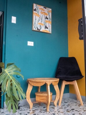 A cozy corner with a framed floral artwork, a stool, and a woven seat, set against a terrazzo floor.