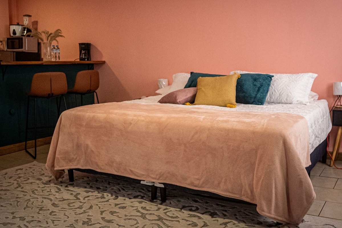 Un dormitorio con cama, escritorio, dos sillas, microondas y mesita de noche.