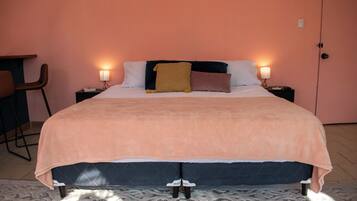 A neatly made bed with a peach-colored blanket, two bedside lamps, and a chair to the left.