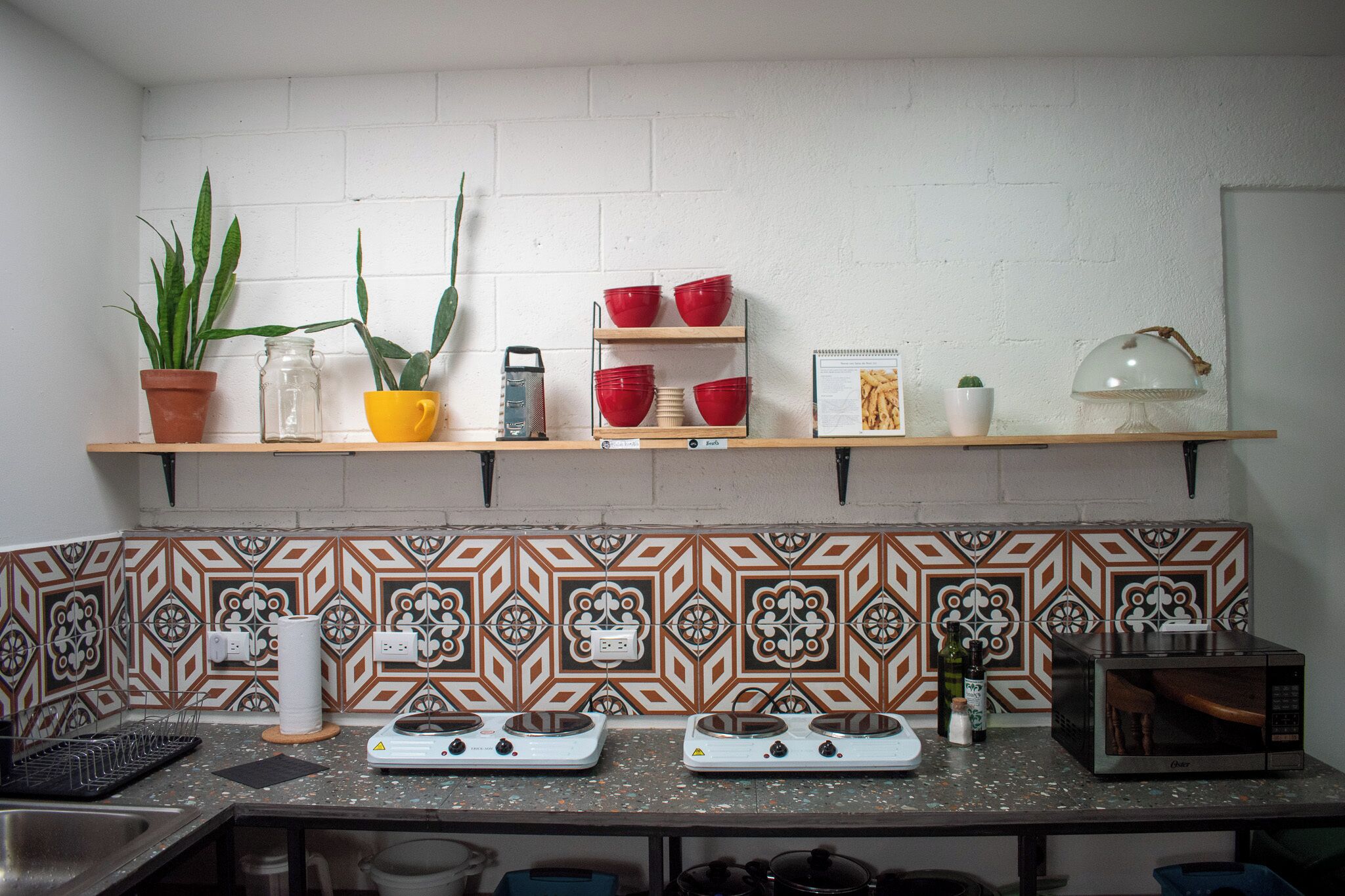 A kitchen with a backsplash of patterned tiles, a stove, a microwave, and shelves with various kitchen items.