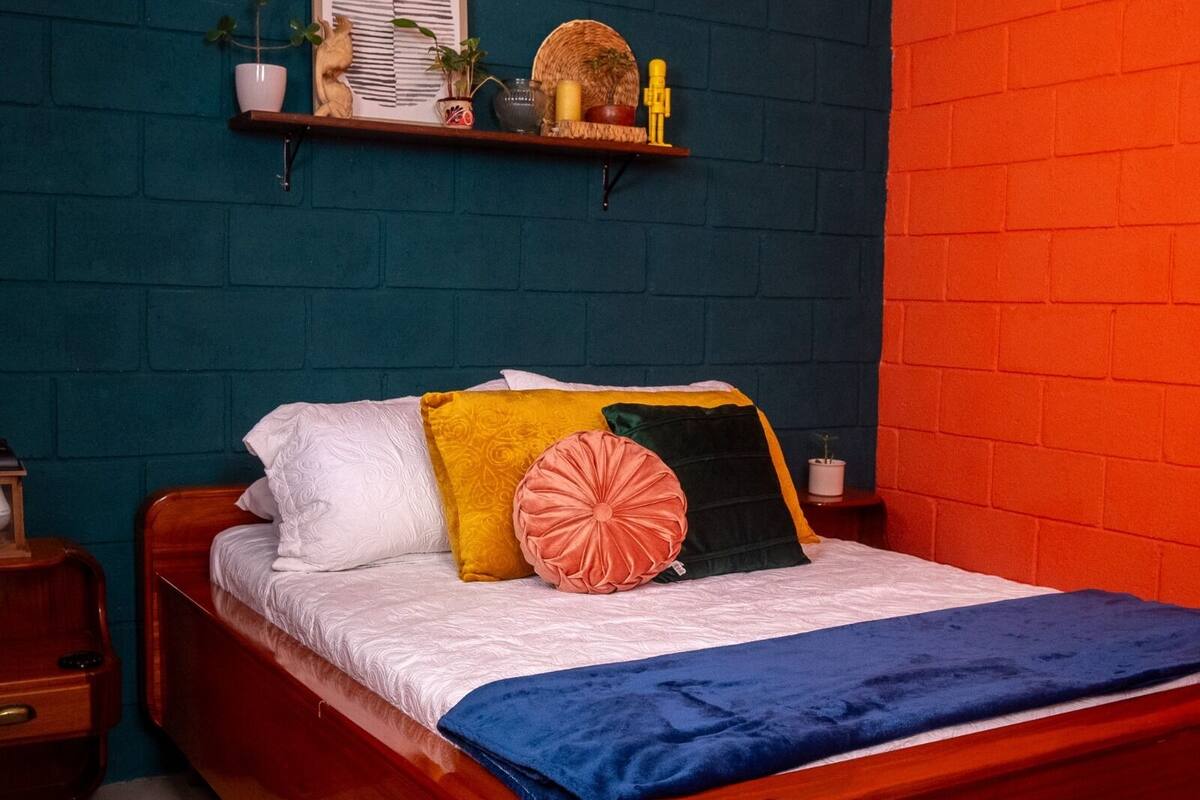 Una cama con una colcha azul, almohadas blancas y amarillas, y un cabecero de madera.