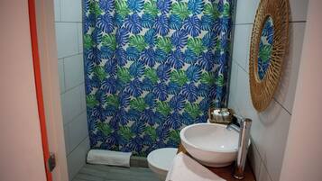 Casa de banho com sanita, lavatório e cortina de chuveiro estampada com folhagem tropical.