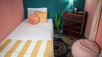 Una cama con un edredón a rayas, una mesita de noche con una lámpara, una planta en maceta y una alfombra estampada.