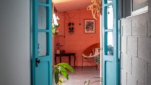 A narrow hallway with a teal door leading to a room with a brick wall, a hanging light fixture, and a hammock chair. - Lolas Hostal (San José)