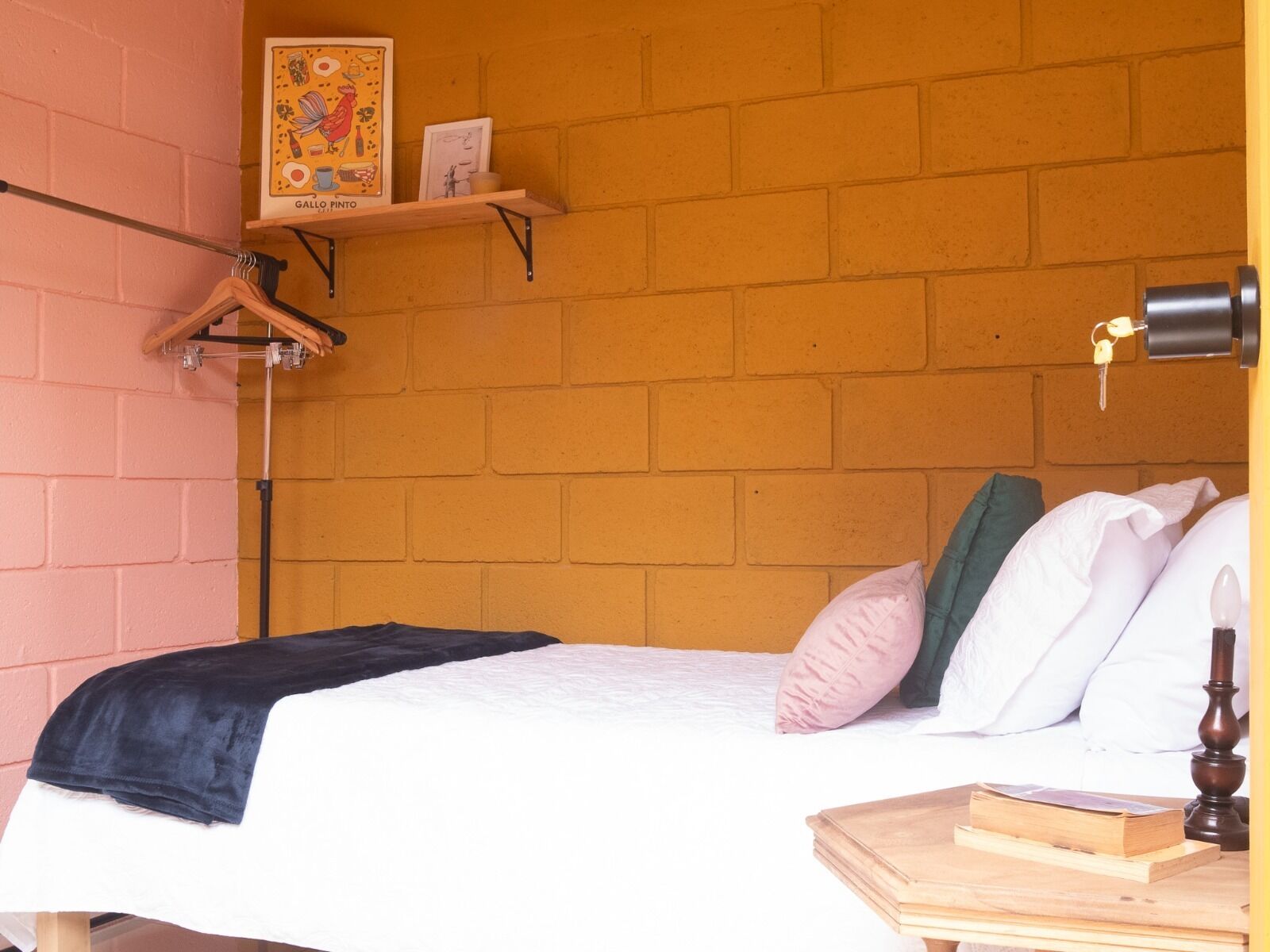 A bedroom with a brick wall, a bed with white bedding, a wooden nightstand, and a shelf with a framed picture.