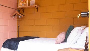 A bedroom with a brick wall, a bed with white bedding, a wooden nightstand, and a shelf with a framed picture.