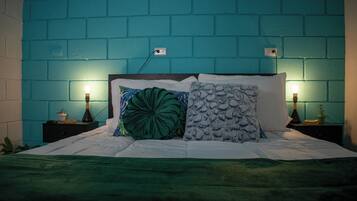 A bed with a green blanket, two nightstands with lamps, and a teal brick wall.