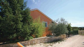 Un bâtiment d’un seul étage, doté d’un toit en pente, entouré d’une végétation luxuriante et d’un mur de pierre.