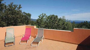 Une terrasse sur le toit, avec trois chaises longues et une vue sur la mer et les collines.