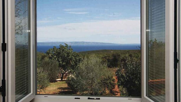 Une fenêtre donnant sur un paysage côtier, avec des arbres et une vue lointaine sur la mer.