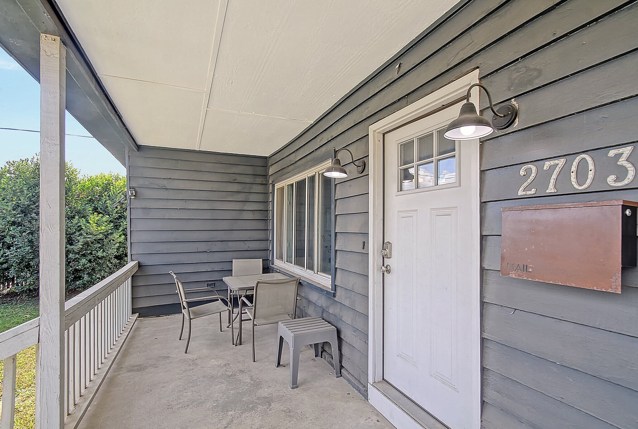 A porch with a white door, a mailbox, and a table with chairs.