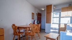 A compact kitchen with wooden furniture, a dining table, and a built-in microwave. - Appartement Aldeïa - Welkeys (Huez)