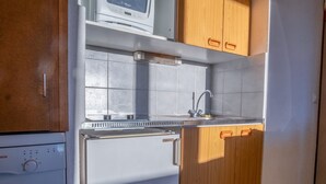 A compact kitchen with a built-in microwave, a sink, and wooden cabinets. - Appartement Aldeïa - Welkeys (Huez)