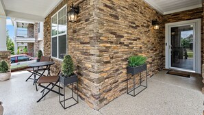 A covered patio with stone walls, a dining table, chairs, and potted plants. - Elegant Home with Large Yard (Nashville)