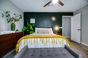 A bedroom with a bed, bedside table, lamp, and a large green plant.