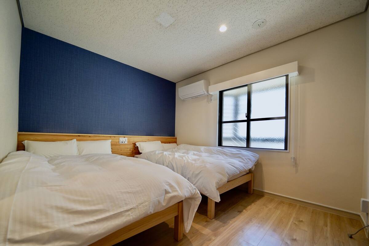 Un dormitorio con dos camas, un ventanal amplio y una pared de acento azul.