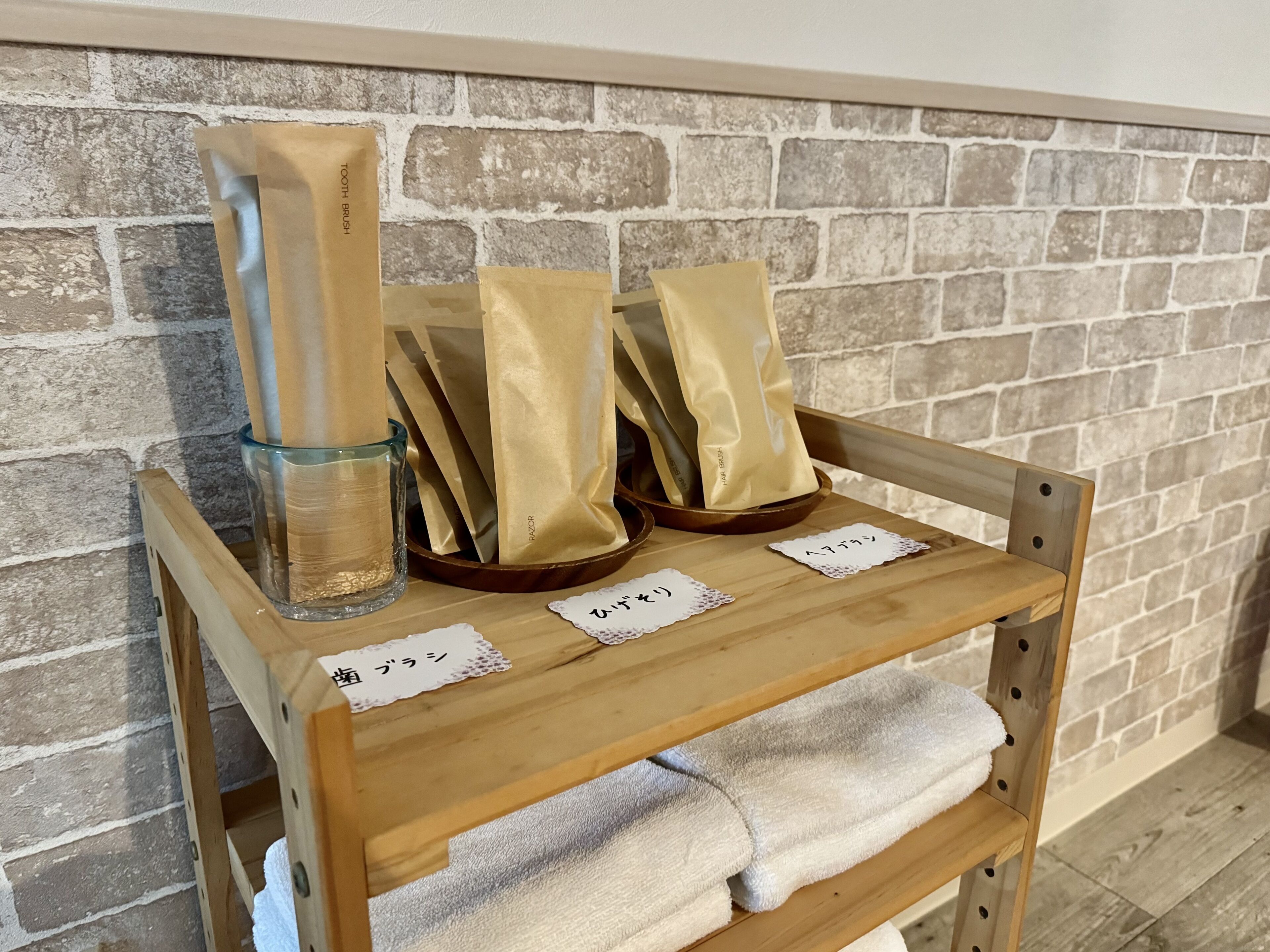 Un estante de madera con un recipiente de vidrio, varias bolsas etiquetadas con texto japonés y una toalla blanca.