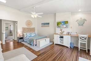 Un dormitorio con cama, mesita de noche, ventilador de techo y vista a la playa.