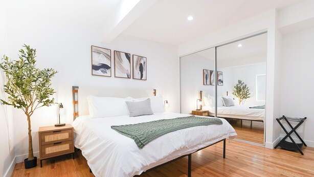 Une chambre moderne avec un grand lit, un plancher en bois, une table de chevet avec une lampe et une plante en pot.
