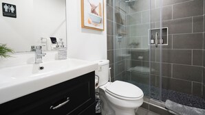 Une salle de bain moderne avec un lavabo blanc, un meuble-lavabo noir, une cabine de douche en verre et un tableau encadré représentant un chien accroché au mur.