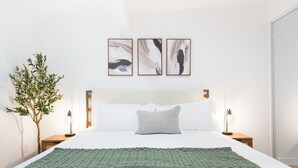 Un lit bien fait, recouvert d’une couverture verte, avec des oreillers blancs et deux tableaux abstraits accrochés au-dessus.