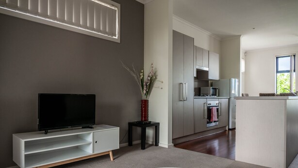 A modern kitchen with white cabinets, a built-in oven, and a microwave. - Tasha's Apartments on Kerry (Athol Park)