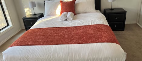 A neatly made bed with white linens and a red throw blanket, flanked by two nightstands with lamps, in a room with a large window.