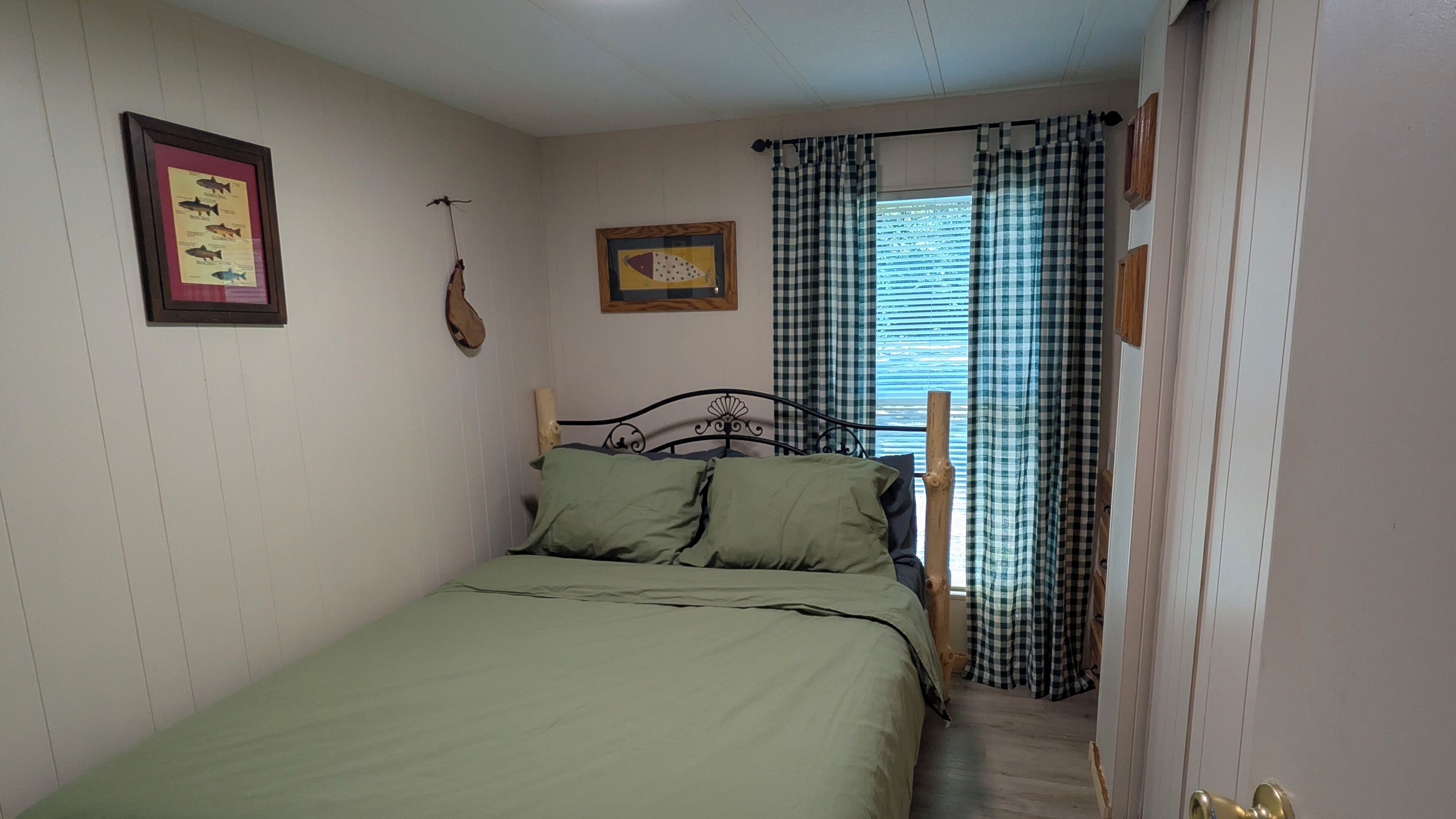 Ein kleines, gemütliches Schlafzimmer mit einem Einzelbett, einer gerahmten Fischkarte und einem Fenster mit Karomustertvorhängen.
