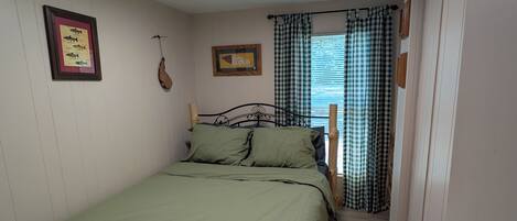 Ein kleines, gemütliches Schlafzimmer mit einem Einzelbett, einer gerahmten Fischkarte und einem Fenster mit Karomustertvorhängen.