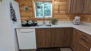 Eine kleine Küche mit Holzausstattung, einem weißen Kühlschrank, einer Spüle und einer Kaffeemaschine.