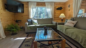 Ein gemütliches Blockhauszimmer mit einer Couch, einem Glastisch und einem an der Wand befestigten Fernseher.