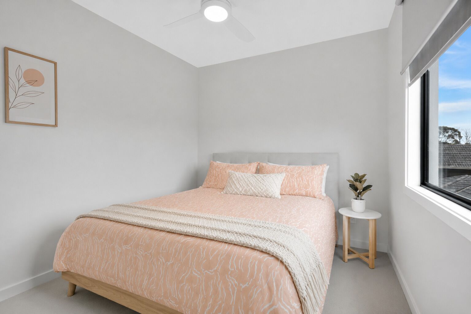 Une chambre à coucher avec un lit, une table de chevet ornée d’une plante, un ventilateur de plafond et une fenêtre donnant sur un beau paysage.