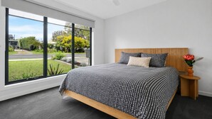 Ein modernes Schlafzimmer mit großem Fenster, einem Bett mit gestreifter Bettwäsche, einem hölzernen Kopfteil und einem kleinen Nachttisch mit einer Vase.