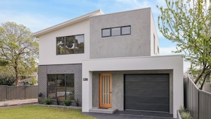 Ein modernes, zweigeschossiges Haus mit Garage, Eingangstür und kleinem Vorgarten.