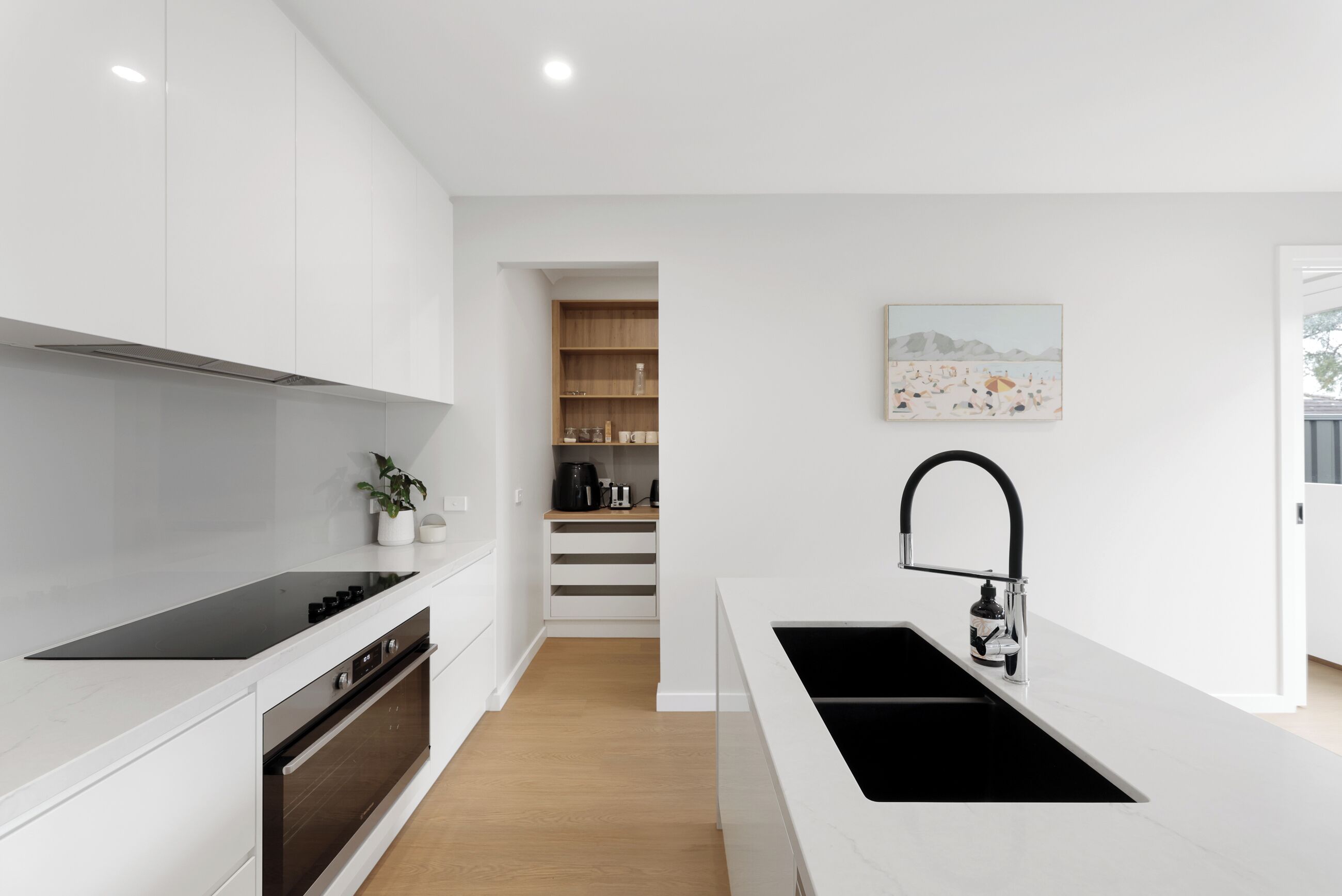 A modern kitchen with white cabinetry, a black sink, and a wooden floor.