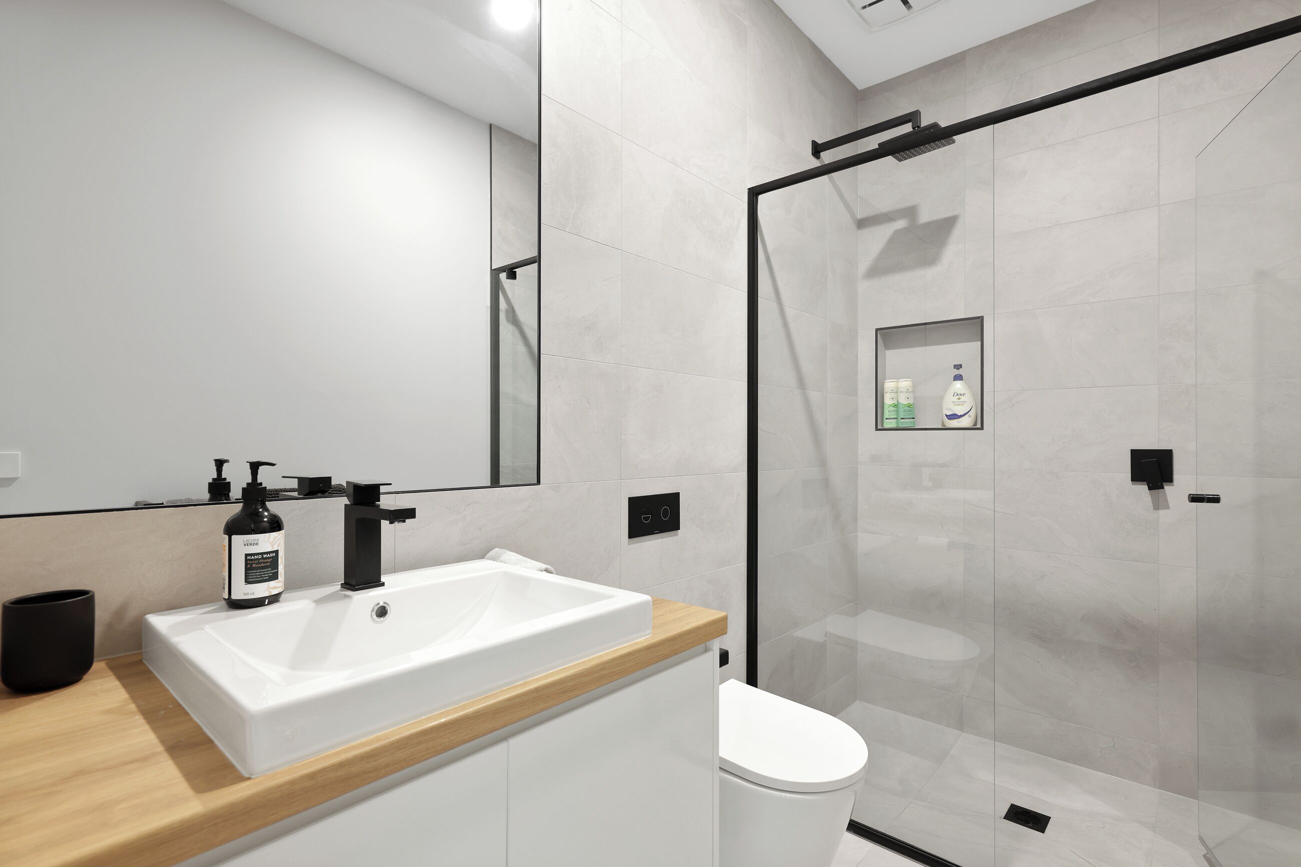 Ein modernes Badezimmer mit Waschbecken, Holzplatte und einer Duschkabine aus Glas.
