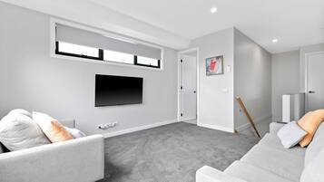 A modern living room with a grey carpet, a flat-screen TV mounted on the wall, and two grey sofas with cushions.