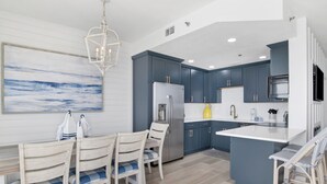 A modern kitchen with blue cabinets, a stainless steel refrigerator, and a large island with bar stools. - Beachfront 1BR + Bunk Alcove @ Phoenix East • Sleeps 6 • Amazing Views & Resort Amenities (Orange Beach)