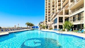 A swimming pool with clear blue water, surrounded by lounge chairs and a tall building with balconies. - Beachfront 1BR + Bunk Alcove @ Phoenix East • Sleeps 6 • Amazing Views & Resort Amenities (Orange Beach)
