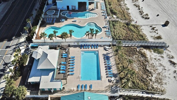 Vista aérea de un hotel con una piscina grande, acceso a la playa y varios balcones.
