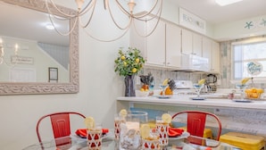 Una cocina moderna con armarios blancos, un espejo grande y una zona de comedor con mesa de vidrio para cuatro personas.