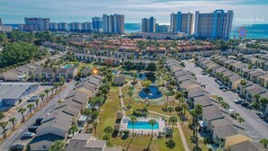 Vista aérea de una zona residencial con propiedades frente al mar, una piscina central y una piscina junto a la playa con parrilla.