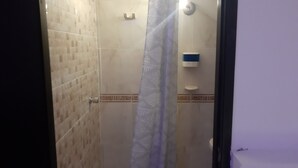 Eine Dusche mit Glastür, gefliesten Wänden und einem blauen Seifenspender.