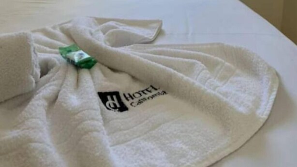 A hotel room with a bed, a window with curtains, and a towel with a logo on it. - Hotel California (Goiânia)