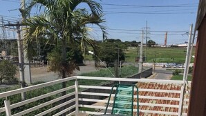 A balcony with a round table and two chairs, a white railing, and a view of a green landscape with a palm tree. - Hotel California (Goiânia)